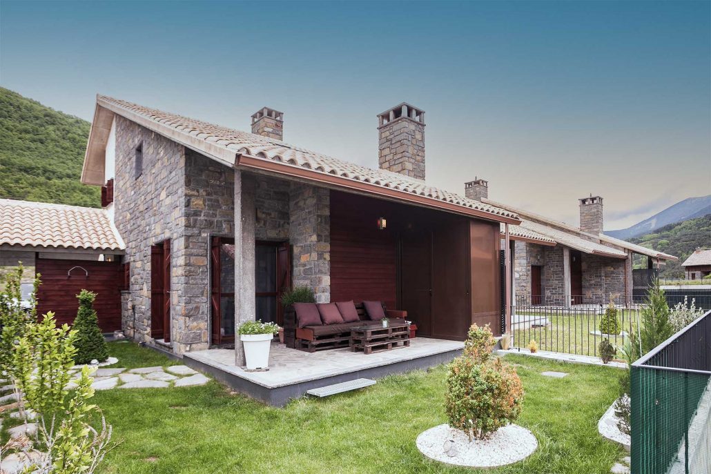 casa-biescas-exterior-1c Fachada de piedra de Casa Biescas con el porche y el jardín cerrado, en Gavín