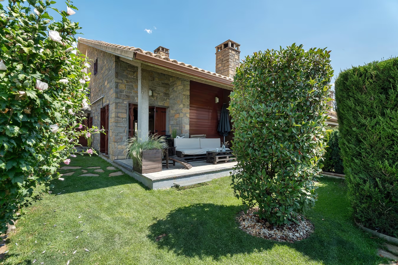 Fachada de piedra de Casa Biescas con el jardín y los setos en verano